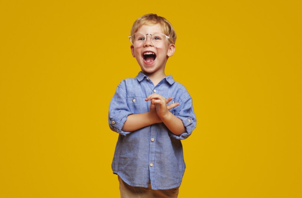 A happy child wearing a pair of glasses with clear frames in front of a yellow background.